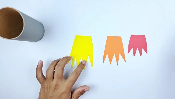 Layer and glue the flame shapes onto the top of the toilet paper roll, yellow at the bottom, then orange, and finally red on top.