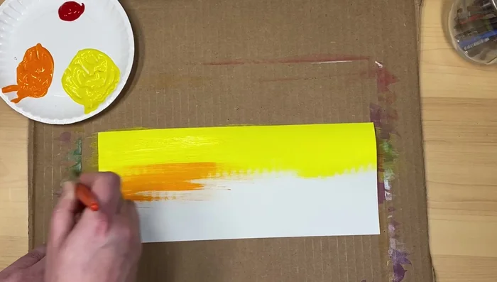 Use your next color (e.g., orange), applying a small amount and spreading it across the paper, blending upwards lightly. Avoid using too much paint at once to make blending easier.