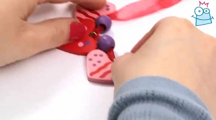 Thread a round purple bead onto each side of the ribbon (near the smaller hearts).