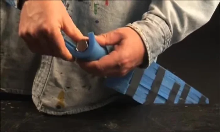 Create the pommel: Cut a 3in wide strip of Camp pad, wrap it around the handle bottom to measure, cut, and bevel one side. Apply glue to the surface and beveled edge, attach carefully, ensuring the bottom edges align. Trim excess and cap with another piece of Camp pad. Repeat two more times for extra layers. Secure with duct tape.