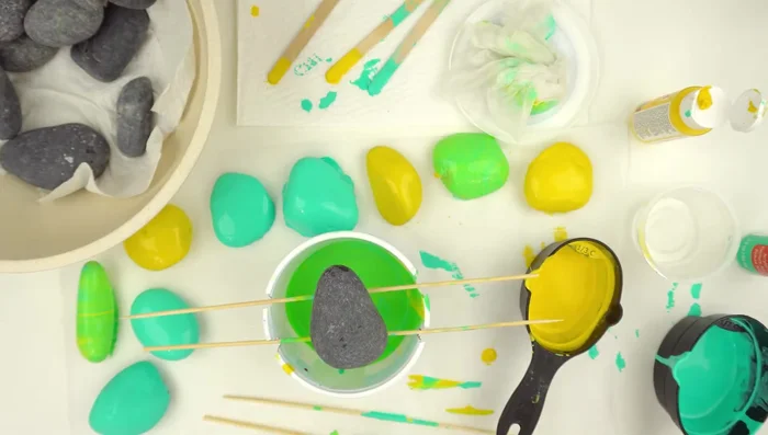 Marble your rocks: Place a base-coated rock on a flat surface. Pour additional colors onto the rock, letting them blend naturally. Use a craft stick to encourage blending and spread if needed.