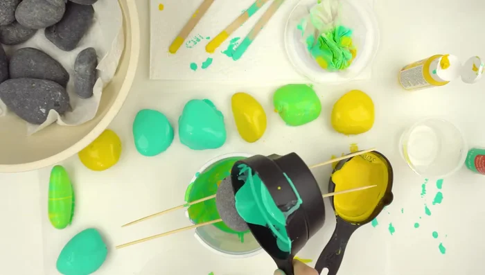 Base coat your rocks: Choose two colors that blend well (e.g., yellow and teal). Pour paint onto rocks placed in the tray.