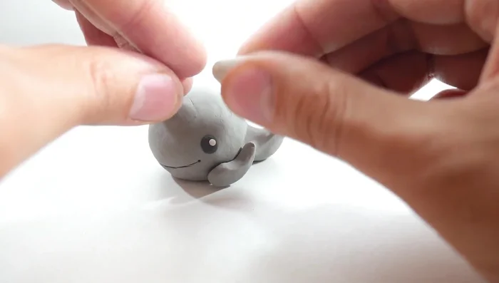 Add the water spout: Create a white clay cylinder, shape the top into a spout, and place it on top of the whale.