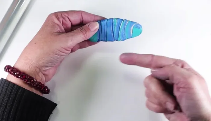 Roll the clay sheet through a pasta machine, perpendicular to the rollers, several times to thin it and blend the colors. Aim for a sheet approximately 4x6 inches and as thin as manageably possible.