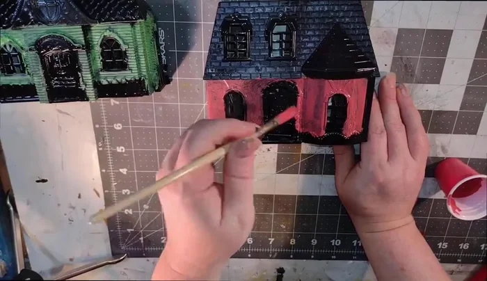 Texturize the red paint on the second dollhouse using a brush with a tapping motion for visual interest.