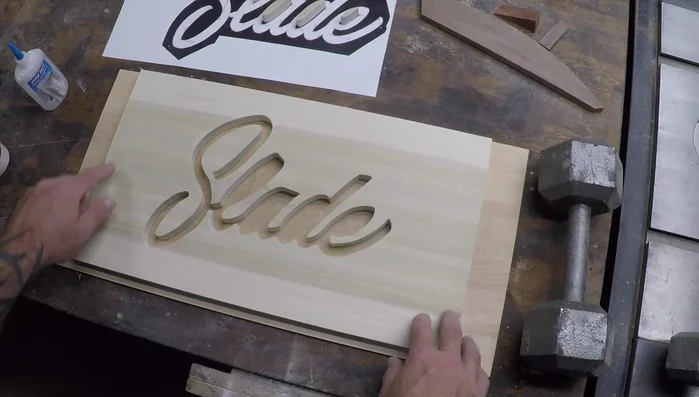 Apply Titebond wood glue to the larger areas and CA glue to the smaller, more delicate parts of the name plaque, and glue the name to the birch plywood backer piece.