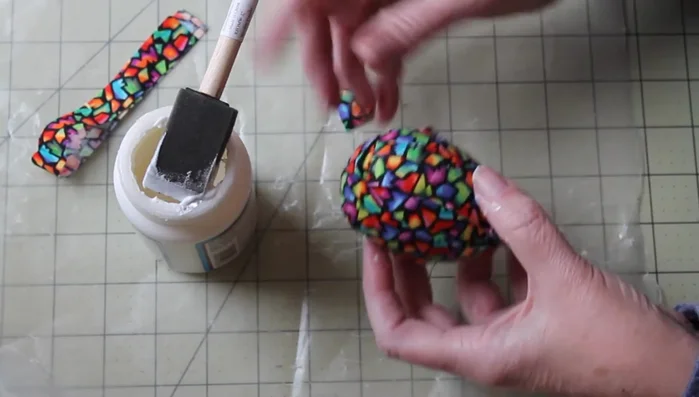 Apply a generous layer of Mod Podge over the entire fabric-covered egg to seal it and create a smooth finish.