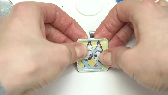 Place the cabochon glass piece over the image, pressing gently to ensure adhesion and remove excess glue with a towel.