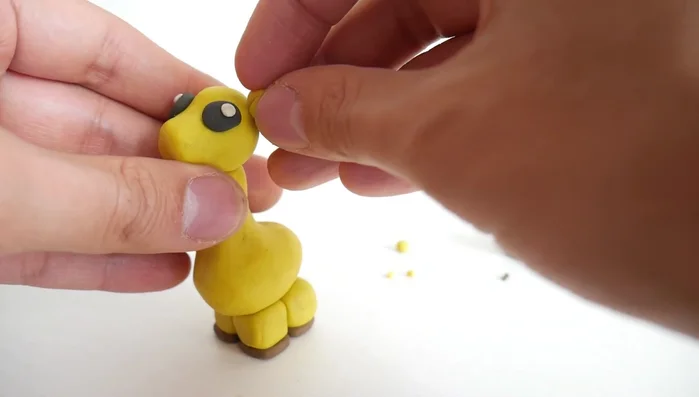 Create horns (ossicones) from small yellow clay strips, adding small brown clay balls to the tips.