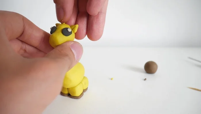 Create horns (ossicones) from small yellow clay strips, adding small brown clay balls to the tips.