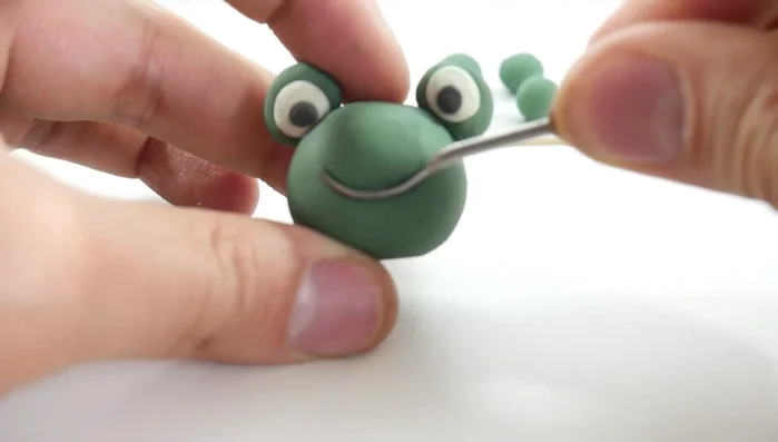 Add facial features: Draw a smile on the frog's head using a pencil or tool. [104.46]