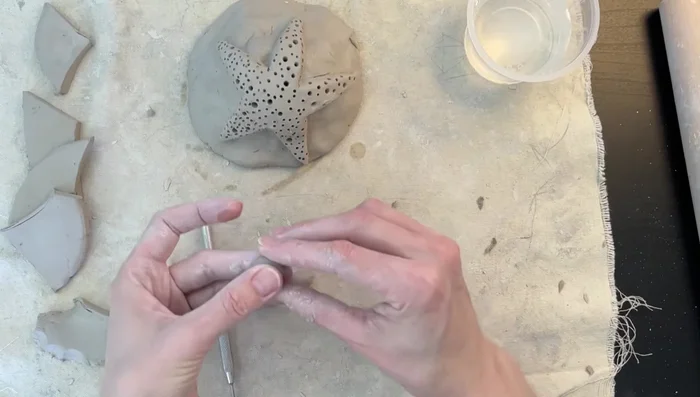 Add sea urchins: Roll small clay balls, flatten slightly, and use a dowel to create a hole in the center. Score and attach the sea urchins to the mound using the score and slip method.