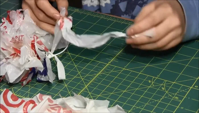 Tie the plastic bag strips onto the wire wreath frame using an over-under knotting technique, similar to tying a shoelace. Push the knots together tightly, adding more strips until the wreath is full.