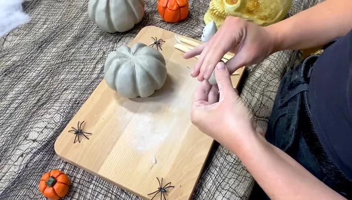Create and attach the stem: Roll a small amount of clay into an oblong shape, molding it into your desired stem shape. Score the base of the stem and the top of the pumpkin, add water, and attach.